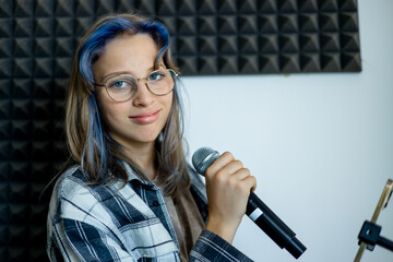 Lifestyle portrait of a teenage girl singing into a microphone in a professional recording studio....