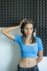 Young woman in a blue crop top and headphones standing in a soundproof recording studio, listening to audio and enjoying the moment. Concept of music, creativity, and media production