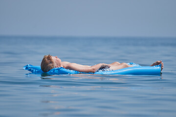 A boy chilling and resting on an air mattress in an ocean in the summer with a blue sky in the background