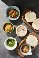 Assorted pita with vibrant dips, bright daylight, arranged overhead on stone and wood