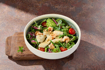 Green salad with squid and shrimp, bright sunlight, overhead ceramic bowl composition