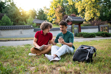 Two teens sitting on the grass and reading books while preparing for lessons