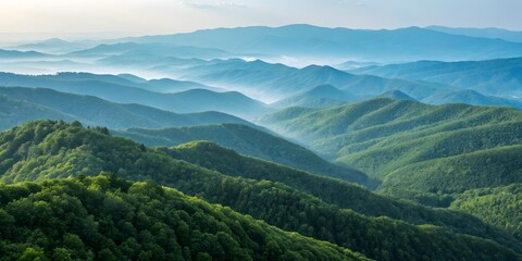 Obraz premium Serene Mountain Vista: A breathtaking panorama unfolds, showcasing layers of rolling mountains shrouded in mist. Verdant slopes meet the clear, blue sky.