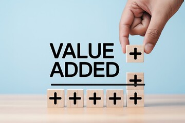 Hand placing a wooden block with a plus sign above the text 'VALUE ADDED,' symbolizing growth, value creation, and the positive impact of contributions.