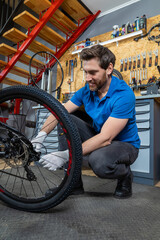 Bearded man servicing bike wheel in indoor workshop surrounded by tools drawers and industrial...