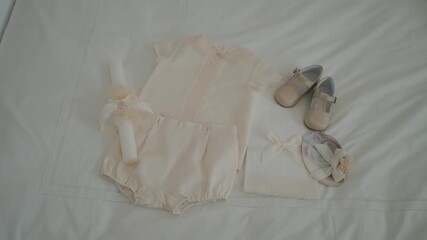 baby christening outfit neatly arranged with matching shoes candle and bonnet on white fabric