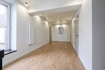 brightly lit, modern hallway features light wood flooring, white walls, recessed lighting, and...