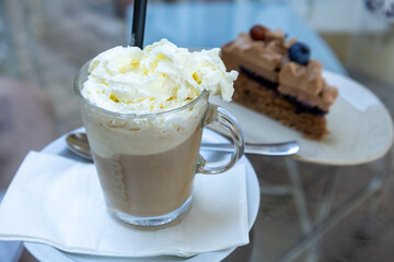 Glass of iced coffee with whipped cream topping and slice of cake
