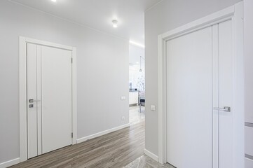 bright hallway with two white doors. The walls are painted light grey, and the floor features...