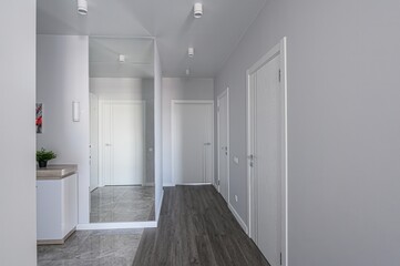 modern hallway with gray walls, white doors, and recessed lighting. A mirror reflects the interior