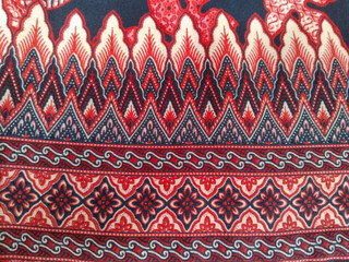 A traditional batik fabric design featuring red and cream leaf patterns with intricate details on a...