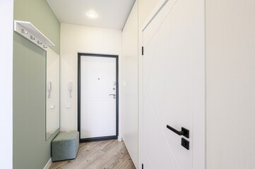 Bright hallway with white doors, a mirror, a soft bench, and wooden floors. Modern and clean design