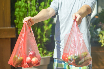 Food delivery service worker holding plastic bags with fresh seasonal fruits and vegetables standing on street on summer day, close-up. Concepts of online grocery shopping, home delivery, e-commerce