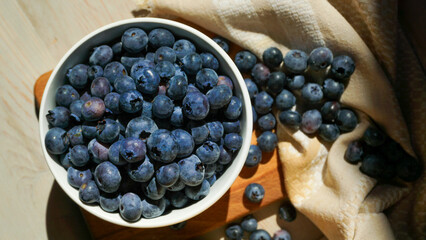 A bowl of ripe blueberries sits on a wooden board with a woven basket in the background, creating a rustic and natural setting ideal for showcasing healthy, fresh, and organic food. Close up