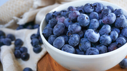 A bowl of ripe blueberries sits on a wooden board with a woven basket in the background, creating a rustic and natural setting ideal for showcasing healthy, fresh, and organic food. Close up