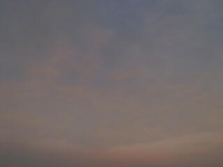 A serene sky at sunrise, transitioning from a deep gray-blue at the top to a muted, soft pink at...