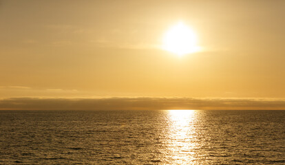The sun is setting over the ocean, casting a warm glow on the water