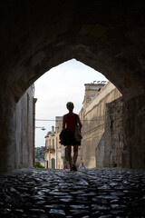 rear view of silhouette of Asian woman walking through arched alley in Matera