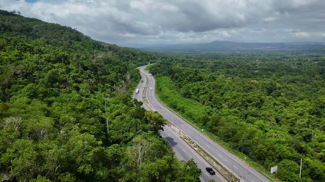 Drone footage of the aerial view of a winding road cutting through lush green forest. Scenic highway number 304 in Thailand links the Bangkok area to Nakhon Ratchasima in the northeastern region