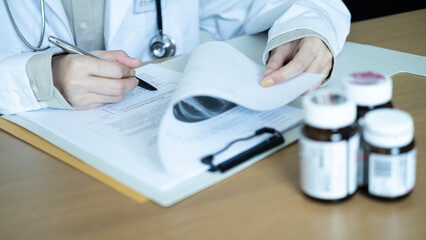 Doctor taking notes on patient report while holding X-ray results, prescription medicine bottles in foreground, representing healthcare and diagnosis process.