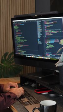 A focused IT engineer typing on a sleek keyboard. Vertical video captures coding on dual monitors, creating a tech-savvy ambiance with warm lighting.