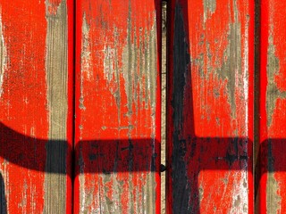 A close-up, abstract photo of a wooden surface with bright red paint that is cracked and peeling,...