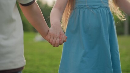 lower view of teenagers holding hands walking through playground grass, casual summer afternoon, friendship bond, relaxed sunlit park stroll, youthful connection, outdoor leisure, cheerful motion - Powered by Adobe