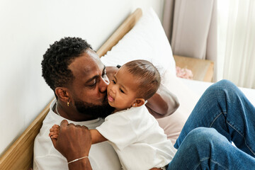 Loving father kisses his smiling baby girl while relaxing on a bed, capturing a warm, authentic moment of family bonding, joy, and affection, perfect for Father’s Day and parenting themes.
