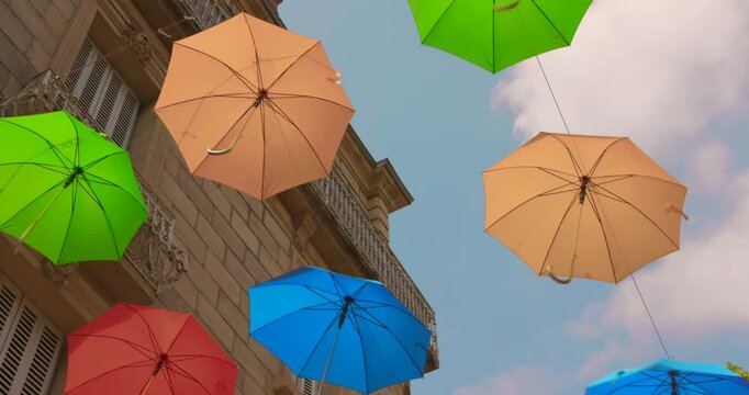 Vibrant summer umbrellas hanging above a historic street in Brive-la-Gaillarde, casting playful shadows on the stone buildings.