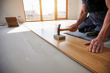 Installing wood flooring. A worker installs new laminate flooring using a hammer and tapping block.