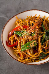 Stir-fried noodles with mixed vegetables and sesame seeds on a ceramic bowl