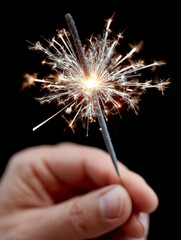 Hand holding a sparkling sparkler on a dark background.