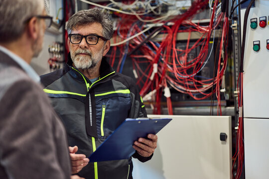 Technician Inspecting Equipment Cables in Electrical Room with Clipboard