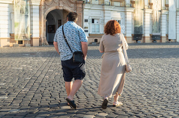 Fat couple walking on the city street and enjoying a sunny day. Rear view of overweight young...
