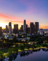Obraz premium City skyline at sunset, reflected in calm water, with green parkland in the foreground
