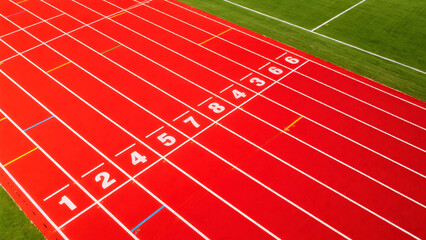 An overhead view of a vibrant red running track, with white lane lines and numbers clearly visible. The image is a high-angle shot, providing a clear perspective of the track. 