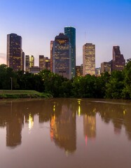 Naklejka premium City skyline reflected in calm, murky water at dusk