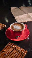 A red cup filled with hot cappuccino topped with leaf latte art, placed on a matching red saucer...