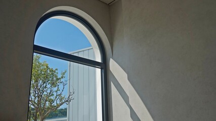 Interior scene with sunlight casting shadows through arched window overlooking modern building