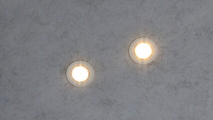 Close-up view of two round recessed ceiling lights glowing warmly on a gray textured surface,...