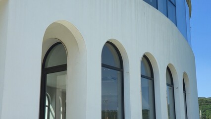 A modern white curved building featuring tall arched windows, smooth facade design, and glass details against a clear sky.