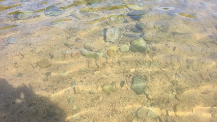 Close-up of transparent shallow river water with visible rocks, pebbles, and sand