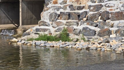 Close-up of a stone embankment wall with concrete water outlet beside a river