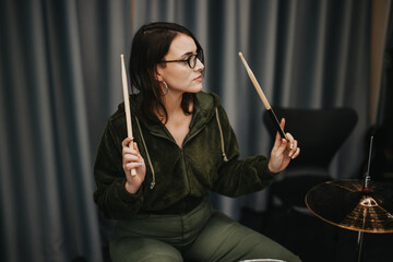 A female musician focuses on playing a drum set while recording in an acoustic studio.