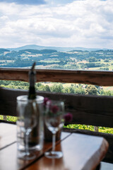 Wine glasses and a bottle sit on a wooden table overlooking a vineyard and rolling countryside. Vineyard dining, wine tasting experience, gourmet rural tourism, slow food
