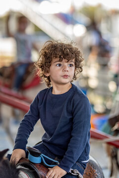 Young boy with curls riding pony at outdoor fair
