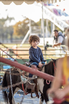 Young boy sits on pony at sunny fairground.
