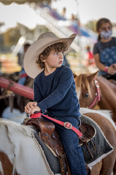 Child in cowboy hat riding pony at outdoor fair carousel