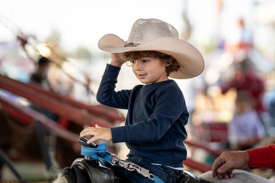 Young boy in cowboy hat rides pony at a fairground attraction