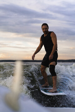 Man wakesurfing on a board in the lake  behind the boat during sunset